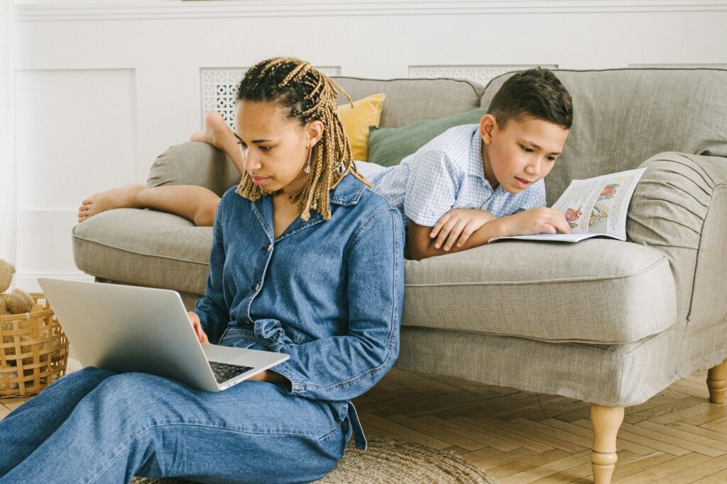 mamans-qui-travaille-sur-un-ordinateur-et-enfant-qui-lit-derriere-sur-le-canape